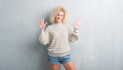 Young blonde woman with curly hair over grunge grey background showing and pointing up with fingers number ten while smiling confident and happy.