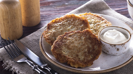 Fried potato pancakes with sour cream on wooden background