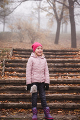 Girl in a pink jacket walking in an autumn misty forest in park