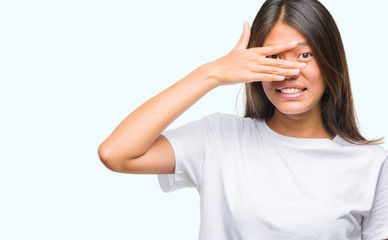 Young asian woman over isolated background peeking in shock covering face and eyes with hand, looking through fingers with embarrassed expression.