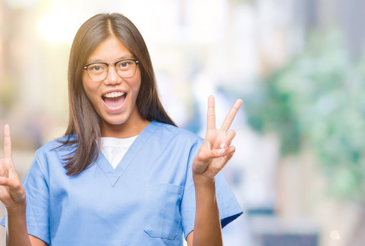 Young asian doctor woman over isolated background smiling with happy face winking at the camera doing victory sign. Number two.