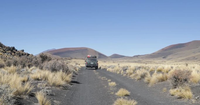 Van in Payunia National Park. Volcanic zone made of lapillis. Background of Herradura Volcano and red, black and golden mountains. Camera stays still while car moves. Malargüe, Mendoza, Argentina
