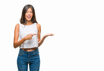 Young asian woman over isolated background amazed and smiling to the camera while presenting with hand and pointing with finger.