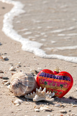 A festive setting of a christmas ornament, a whelk and a starfish at the beach with a wave at low tide along Barefoot Beach, Florida.