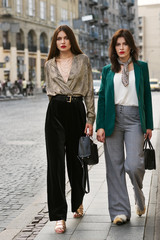 Outdoor full body portrait of two young beautiful fashionable women wearing stylish trendy clothes,...