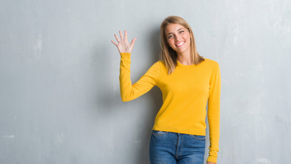 Beautiful young woman standing over grunge grey wall showing and pointing up with fingers number...