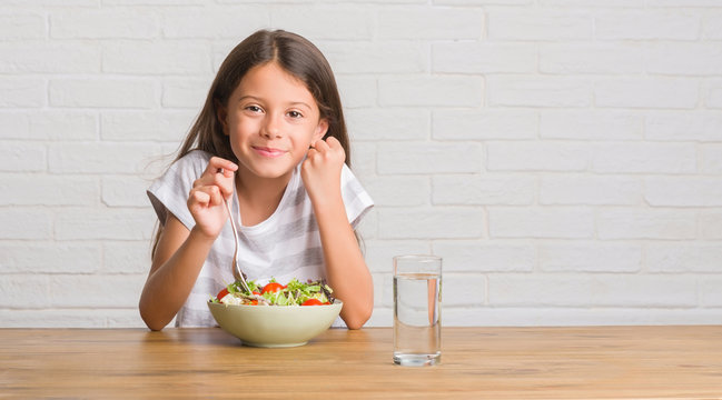 Young Hispanic Kid Sitting On The Table Eating Healthy Salad Screaming Proud And Celebrating Victory And Success Very Excited, Cheering Emotion