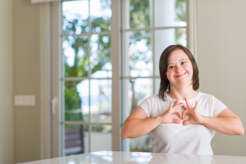 Down syndrome woman at home smiling in love showing heart symbol and shape with hands. Romantic...