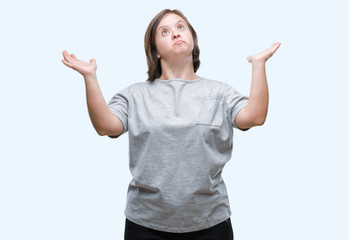 Young adult woman with down syndrome over isolated background clueless and confused expression with arms and hands raised. Doubt concept.