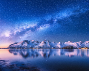 Bright Milky Way over snow covered mountains and sea at night in winter in Norway. Landscape with...