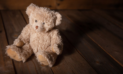 Teddy bear sitting on floor, dark empty wooden background, copy space