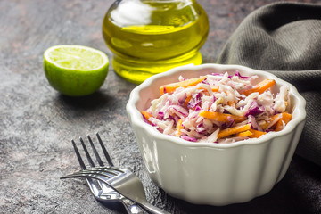 Fresh coleslaw salad made of shredded red and white cabbage and carrots, served in bowl, on dark background