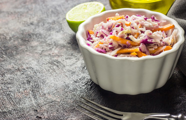 Fresh coleslaw salad made of shredded red and white cabbage and carrots, served in bowl, on dark background
