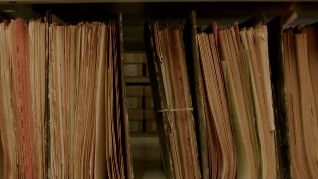 Camera movement along a file shelf. The files are old, the paper is yellowed.