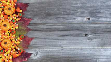 Left border of Halloween trick or treat candies plus autumn decorations on rustic wooden boards