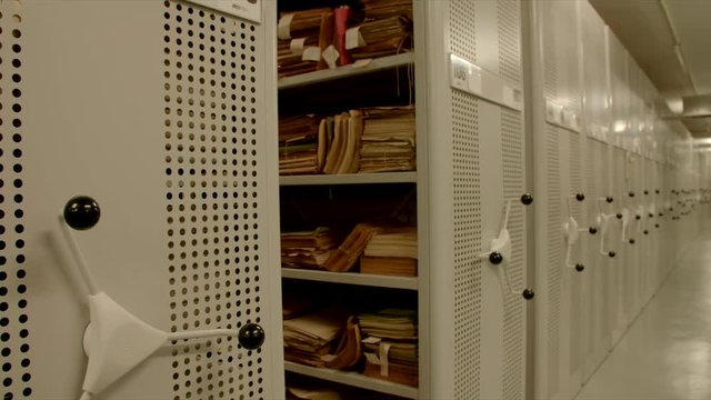 In an archive with relocation shelves, the camera moves to a shelf inside with old files. The image can be used for the integration of archive texts in films and reports. 