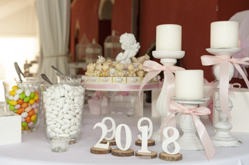 Glass vases fill up with sugared almod, white candels and party favor, above white tablecloth
