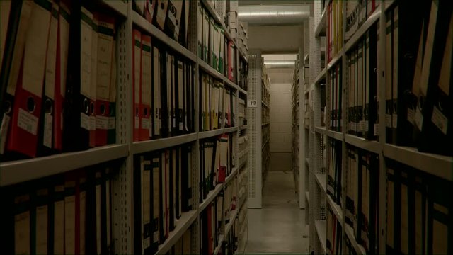 Slow camera movement between two archive shelves filled with folders. The image can be used for the integration of archive texts in films and reports. Thanks to the 50 frames it can be slowed down.