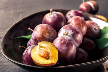 Whole fresh red violet blue plums and slices cut with knife in bowl on kitchen table