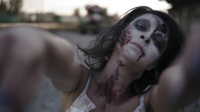 Portrait of a creepy zombie woman with wounded face walking outdoors with an industrial abandoned place on the background. Halloween, filming, creepy concept