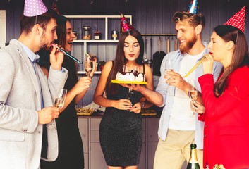 Charming female blowing on candles on birthday cake after making her wish at party.