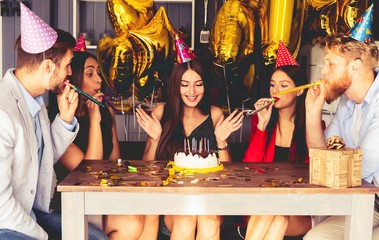 Charming female blowing on candles on birthday cake after making her wish at party.