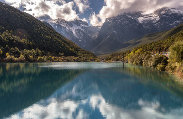 Yulong snow mountain range with it reflection in turquoise lake surrounded by pine forest mountain in cloudy day at Lijiang, Yunnan, China