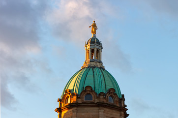 A statue of an angel sitting at the top of the dome of the Mound Museum in Edinburgh, Scotland, UK at sunset.
