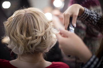 Curling tongs in the hands of a woman. Female hairdresser standing and making hairstyle to cute lovely young woman in beauty salon