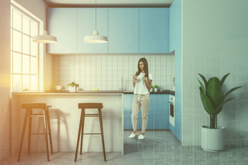 Woman in white tile kitchen, blue countertops