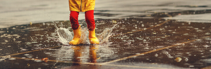 legs of child   with rubber boots jump in puddle  on autumn walk
