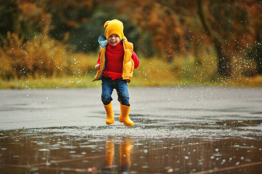 happy child baby boy with rubber boots jump in puddle  on autumn walk