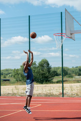 Naklejka premium Side view action shot of African man jumping in basketball court scoring points, copy space
