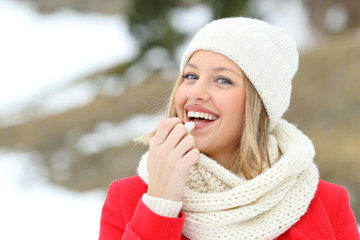 Happy woman applying lip balm outdoors in winter - obrazy, fototapety, plakaty