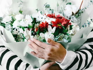 Flower arrangement against white background Close-up photo Woman is holding a large bouquet of flowers in a paper package in her hands