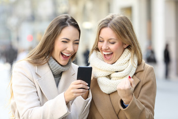 Excited friends reading phone content in winter