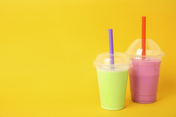 Plastic cups of tasty milk shakes and space for text on color background