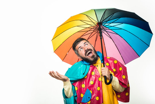 Handsome man wearing in autumn clothes on autumn sunny day. Young attractive man in raincoat under colored umbrella is trying to see if there is rain. Funny face. Autumn boy preparing for Autumn sale.