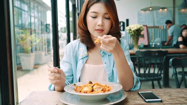 Attractive beautiful Asian woman food blogger using smartphone or camera photo and recording making food vlog video for her subscribers and her channel at cafe and restaurant.