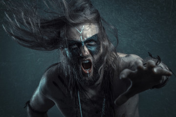 Dark tribal shaman or warlock summoning spirits using a deer skull and his ritual staff, halloween...