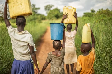  Groep jonge Afrikaanse kinderen die met emmers en jerrycans op hun hoofd lopen terwijl ze zich voorbereiden om schoon water terug naar hun dorp te brengen. © Logan Venture