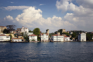 Fototapeta na wymiar View of historical, old Turkish / Ottoman houses and a castle by Bosphorus on Asian side of Istanbul. It is a sunny / cloudy summer day.