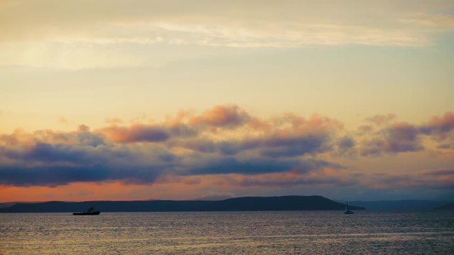 Sea view on a pleasant summer evening: a beautiful sunset, colored clouds, a pure sea with a yacht, the glint of the sun on the water. Sea, ocean, natural video for tourist, resort and meditative site