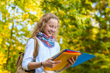 Smiling girl student reading a notebook in the autumn park