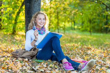 Teen student woman sitting on lawn in park with books and notebook and writes
