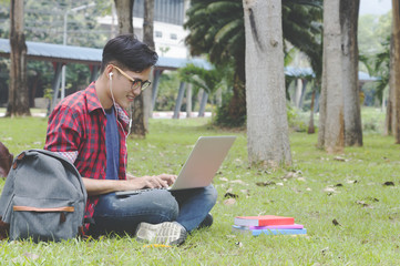 Asian attractive male student thinking about coursework strategy sitting in university garden with laptop computer connected to wireless internet.