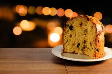 closeup panettone on ceramic plate on wooden table, bokeh background with lights