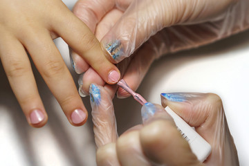 Professional manicure for child. Cosmetologist applies healing and firming varnish on nails on child's fingers. Shooting close-up.