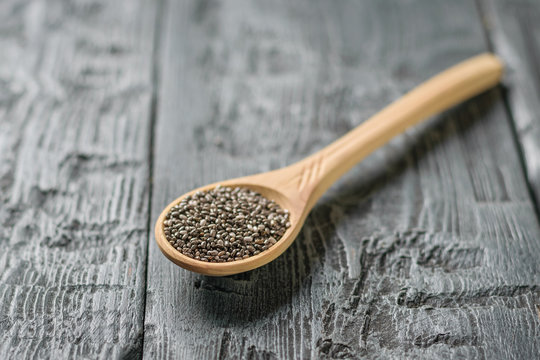 Wooden spoon with Chia seeds on black rustic table.