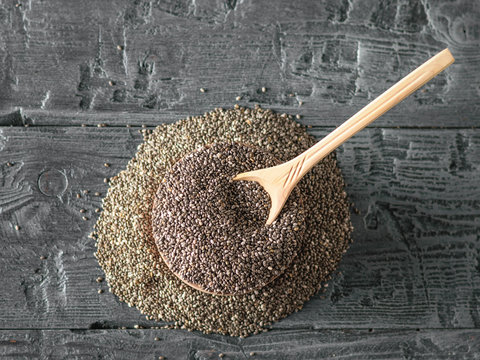 Wooden spoon with Chia seeds on black rustic table. The view from the top. Flat lay.